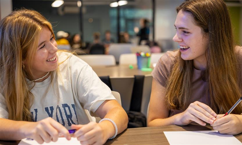 Two students smile while discussing ideas